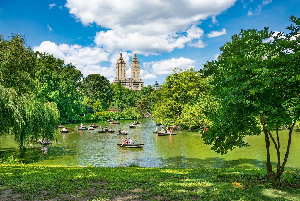 Summer scene in NYC Central Park with boaters on lake.